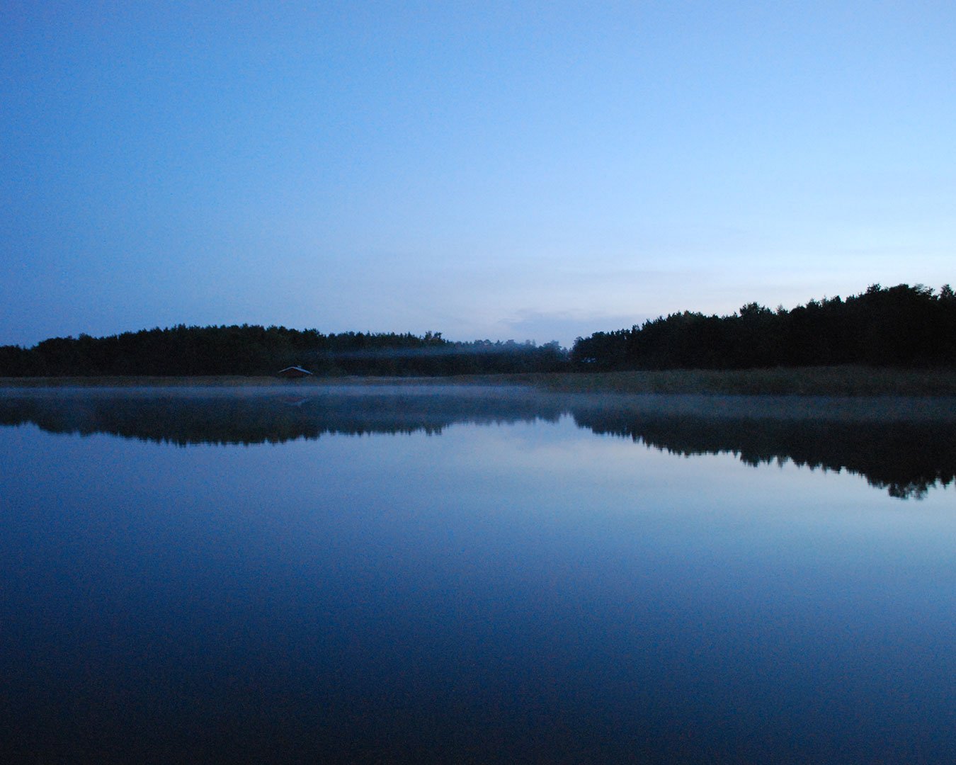 Dawn light over a calm lake with a forested shoreline reflected in still water.