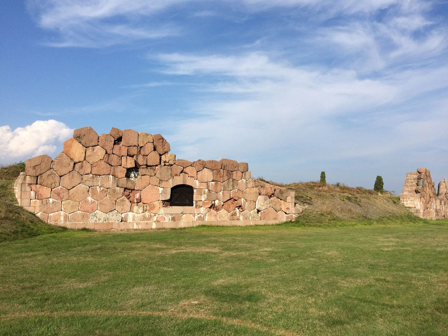 Bomarsund fortress ruins with a stone wall and arched doorway against a clear blue sky.