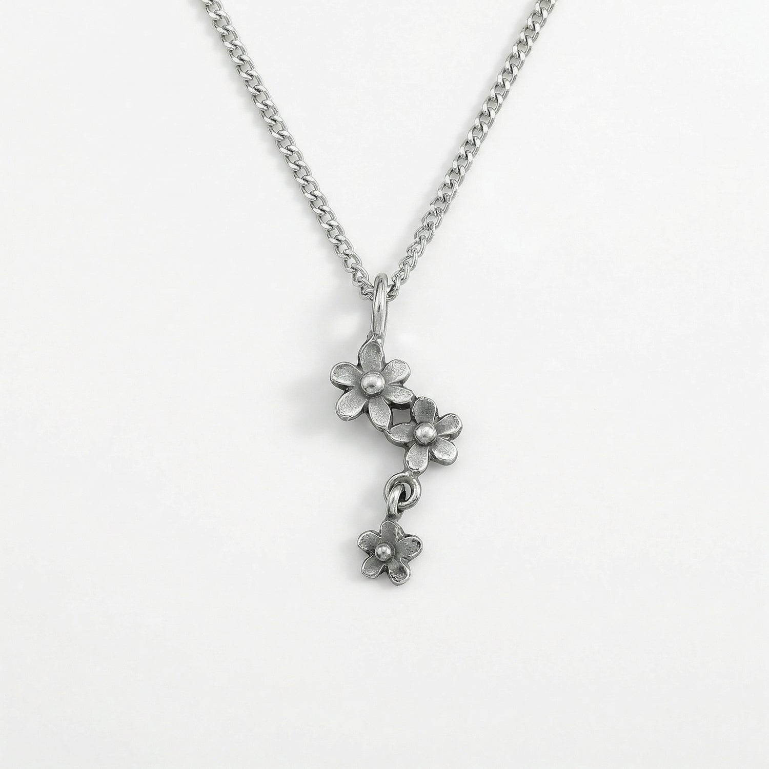 Close up of a silver flower pendant necklace on a chain against a white background.