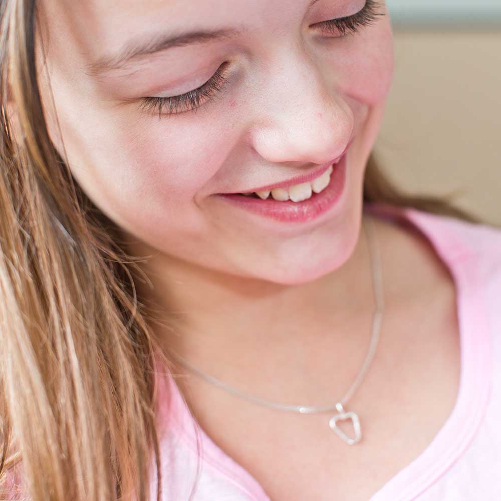 Närbild av person i rosa topp som bär ett silverhalsband med öppet hjärta