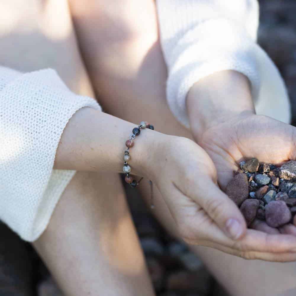 STRAND armband med färgade stenpärlor runt handleden mot en rockig bakgrund