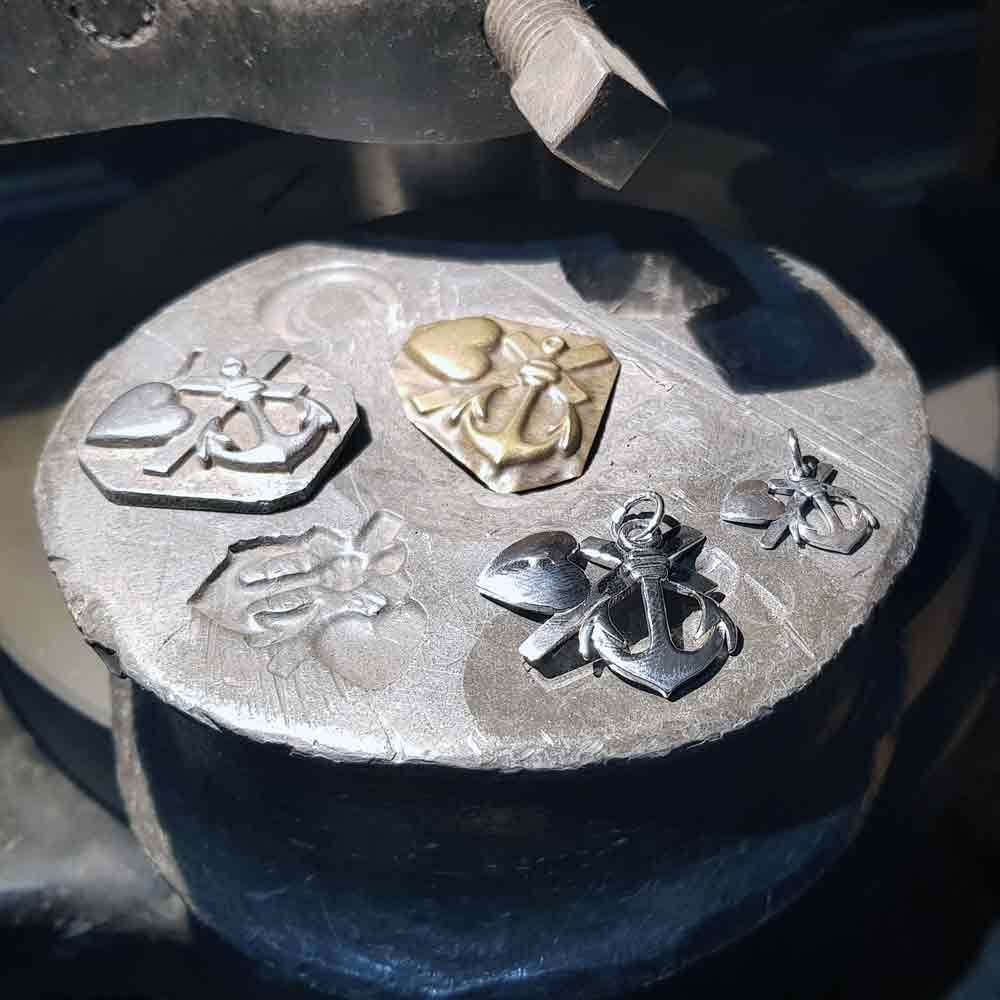 Tre små silver berlocker med hjärtan och ankare motiv på en metallplatta