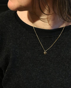 Modell bär ett 18K guld hjärtformigt hängsmycke på tunn kedja runt halsen