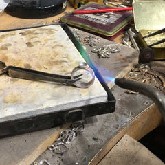 Handmade silver ring in progress on a jeweler's bench with tools and metal scraps