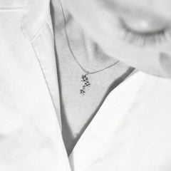 Close up of a silver flower pendant necklace worn on a model against a light top.