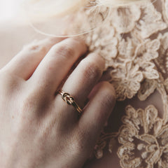 Close up of a gold knot ring worn on a finger with a soft beige textured background