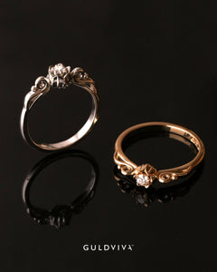 Två Lily of Love ringar i vitt och rosé guld med diamant i blomformad setting mot svart bakgrund