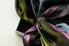 Close-up of a multicolored silk scarf featuring green purple and blue tones secured with a silver decorative ring.