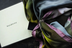 Multicolored silk scarf tied with a decorative silver ring beside a white GULDVIVA box.