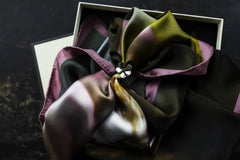 ÄPPELBLOM Scarfring i silver med blomformad design ligger på en färgglad scarf i en öppen låda