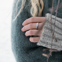 Close up of a hand wearing a textured silver ring with a dark stone against a gray knit sweater