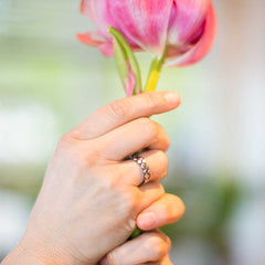 Hand holding a pink tulip wearing a BOMARSUND silver ring with a textured pebble band