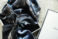 Hemma Hamn silk scarf in blue gray tones tied with a silver ring inside a gift box