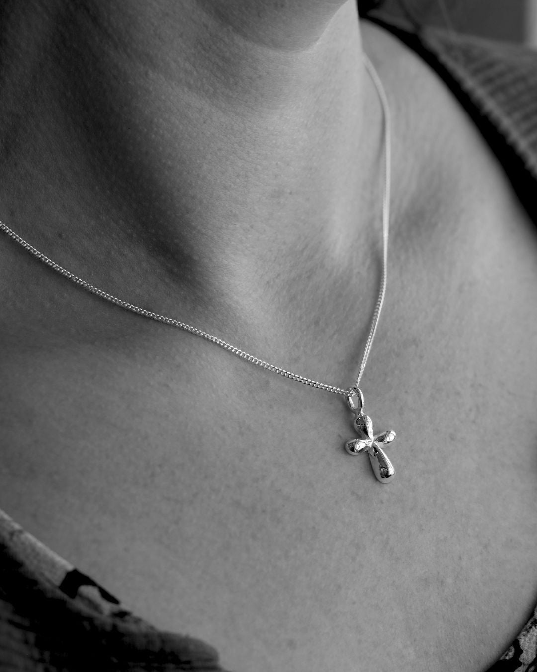 Collier de croix SWEET avec une petite croix en argent aux formes douces, portée autour du cou d'une personne.